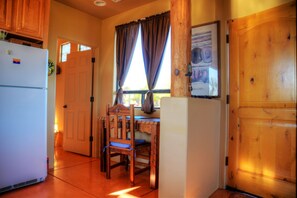 A kitchen with wooden cabinets, a white refrigerator, a dining table with chairs, and a window with curtains.