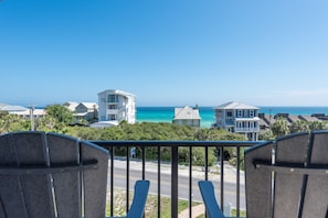 A balcony with two chairs overlooking a coastal view with houses and the ocean.