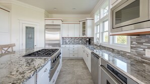 A modern kitchen with white cabinetry, a granite countertop, stainless steel appliances, and a large window providing natural light.