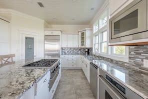 A modern kitchen with white cabinetry, a granite countertop, stainless steel appliances, and a large window providing natural light.