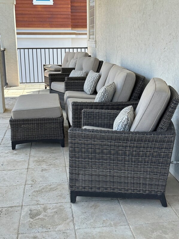 A set of wicker sofas with cushions, positioned on a tiled patio area.