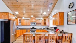 Una cocina con armarios de madera, una isla central con sillas, electrodomésticos de acero inoxidable e iluminación colgante.