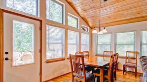 Un comedor con mesa y sillas de madera, ventanas amplias con persianas y un techo con vigas de madera.