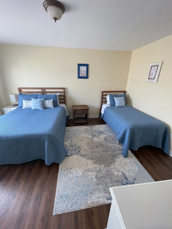 Habitación doble con dos camas, una mesita de noche pequeña, ventilador de techo y alfombra estampada.