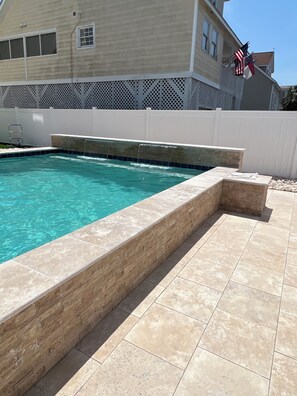 Una piscina con borde de piedra, valla blanca y una bandera estadounidense.