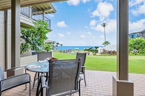 A patio with a table and chairs, a view of the ocean, and a building with a balcony.