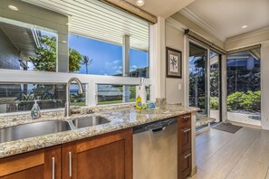 Enjoy cooking in this well-lit kitchen with a granite countertop, stainless steel sink, and dishwasher, offering a view of the outdoor garden.