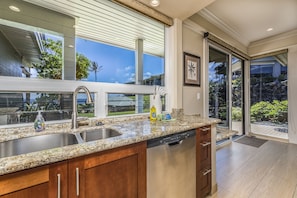 Enjoy cooking in this well-lit kitchen with a granite countertop, stainless steel sink, and dishwasher, offering a view of the outdoor garden.