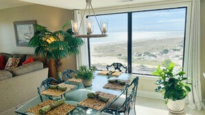 A dining area with a glass table, woven placemats, and a view of the beach.