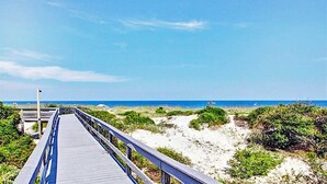 A wooden boardwalk leading to a beach with sand dunes and sparse vegetation.