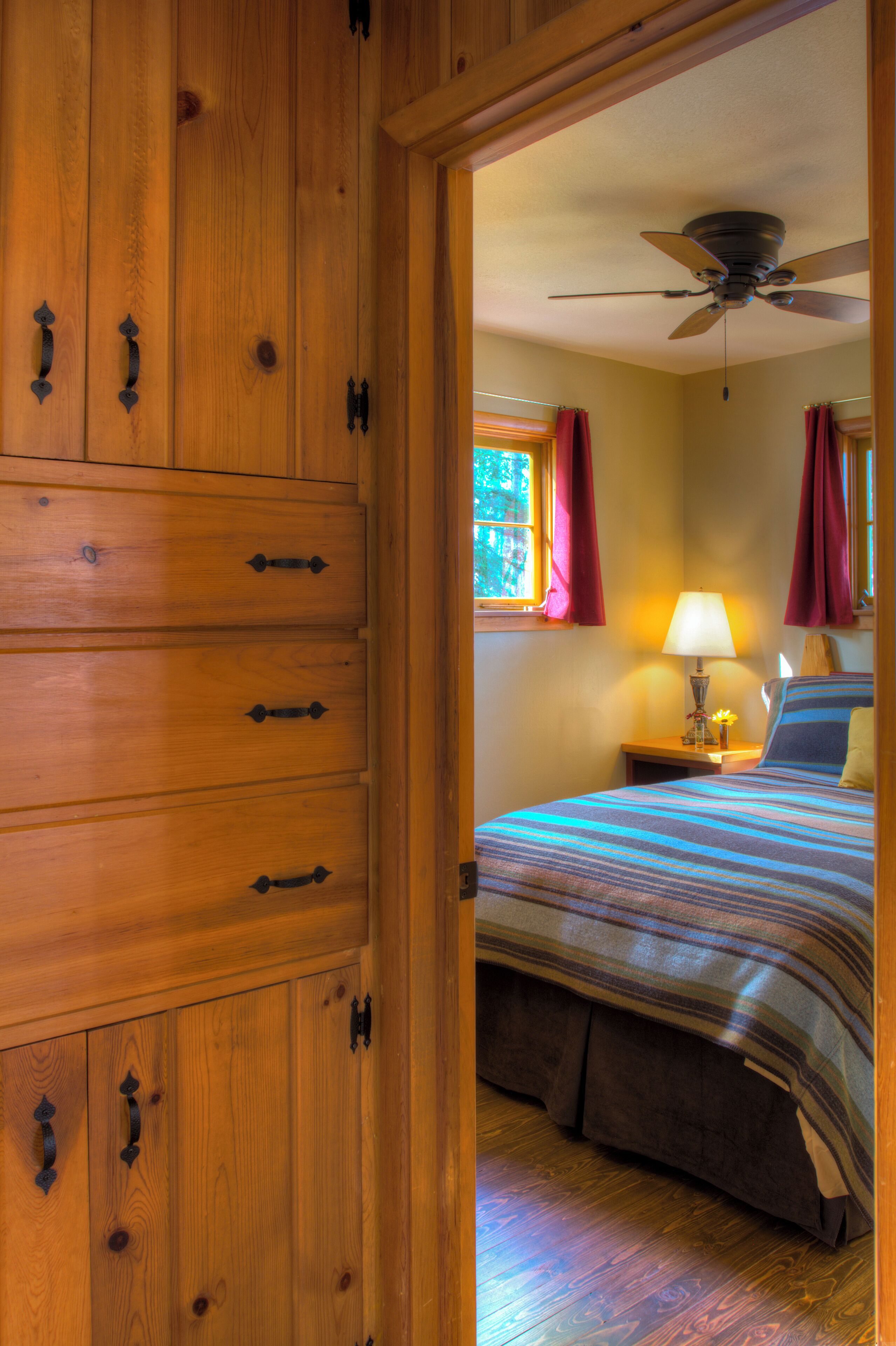 A wooden wardrobe with multiple drawers and a bed with a striped bedspread and a single pillow.