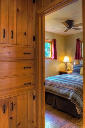 A wooden wardrobe with multiple drawers and a bed with a striped bedspread and a single pillow.