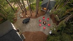 Un área de estar al aire libre circular con un brasero, rodeada por un patio empedrado.