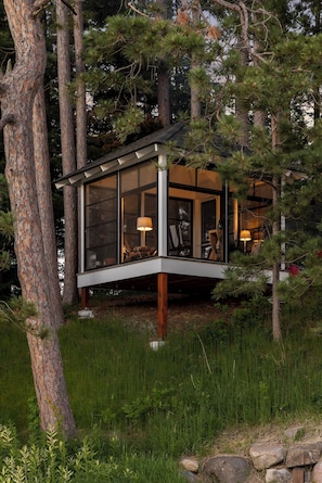 Une cabane moderne dotée de grandes fenêtres, d’une terrasse en bois et d’une véranda en verre.