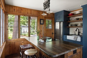 Cocina con armarios de madera, un refrigerador de acero inoxidable, un lavamanos integrado y un amplio ventanal con vistas a árboles.