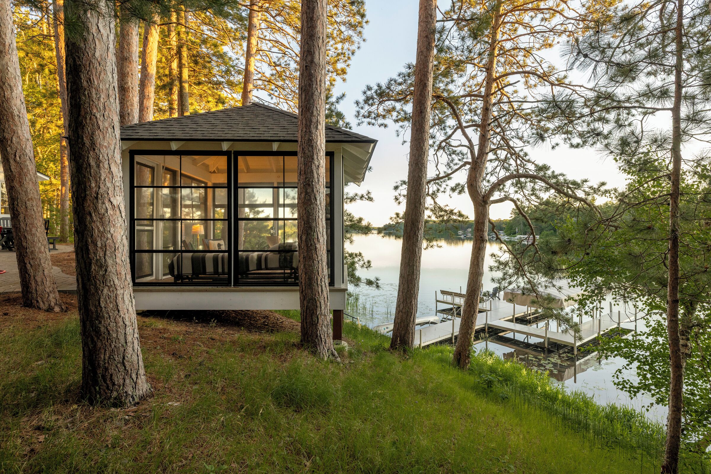 Una cabaña con ventanas amplias que dan a un lago, rodeada de árboles.