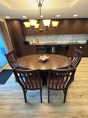 Une table de salle à manger ronde, entourée de six chaises, un lustre, des meubles en bois, un pare-feu en marbre et un lave-vaisselle encastré.