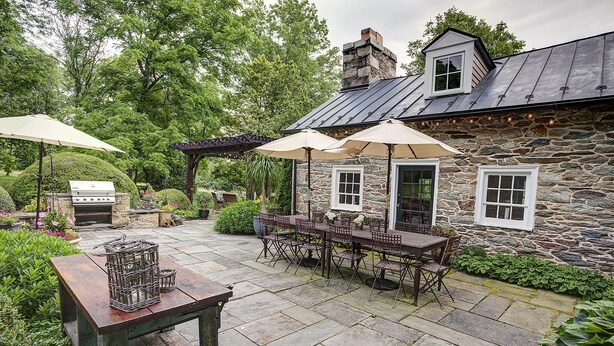 Ein Steinhaus mit einer Terrasse, die einen Grill, Sitzgelegenheiten und Sonnenschirme bietet.
