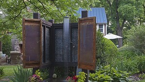 Ein Garten mit Wasserspiel, Holzbanken und Kübelpflanzen.