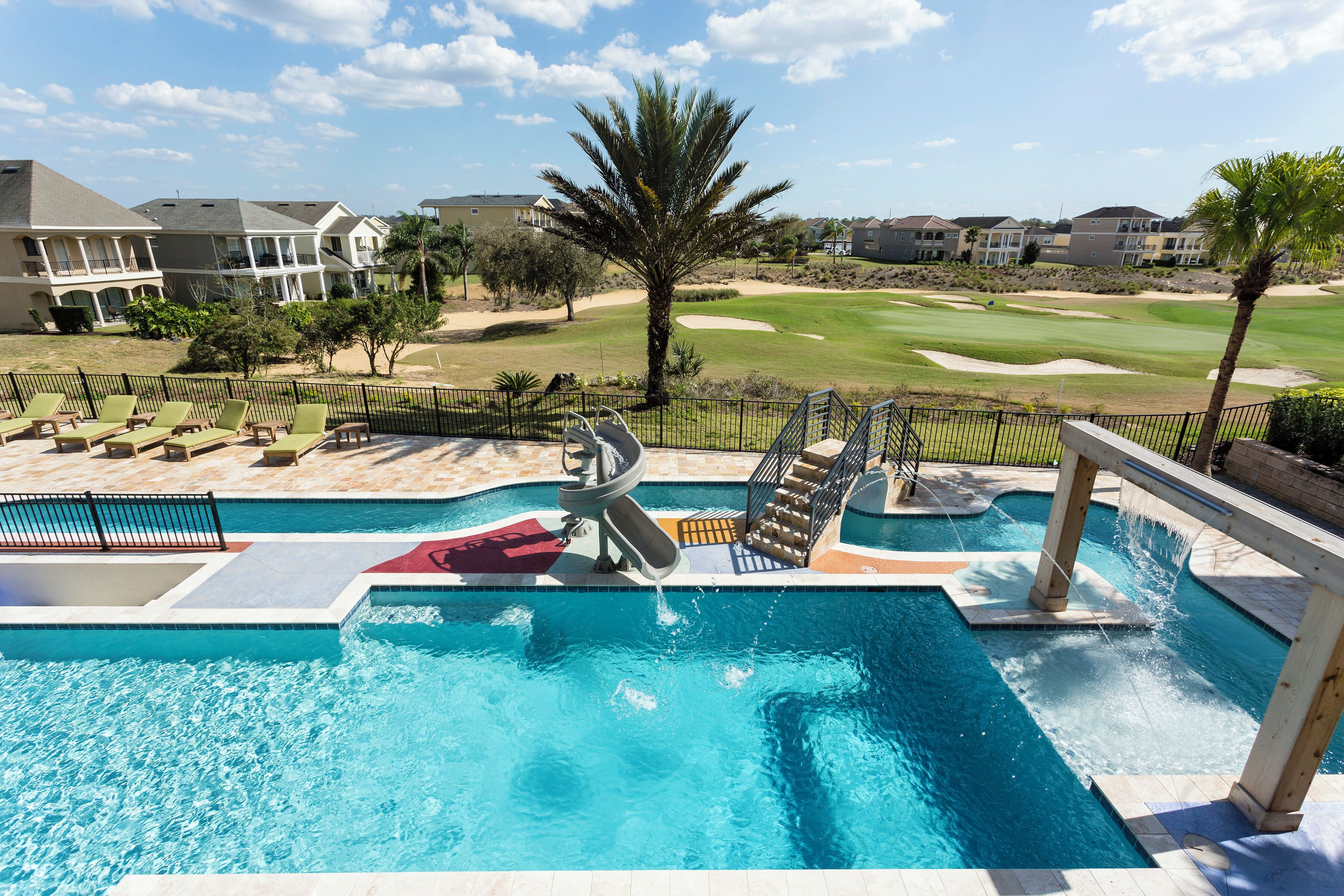 Ein Swimmingpool mit Wasserrutsche, Liegestühlen und Blick auf einen Golfplatz.