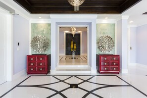 A spacious lobby with a polished floor, two red side tables with decorative vases, and a chandelier.