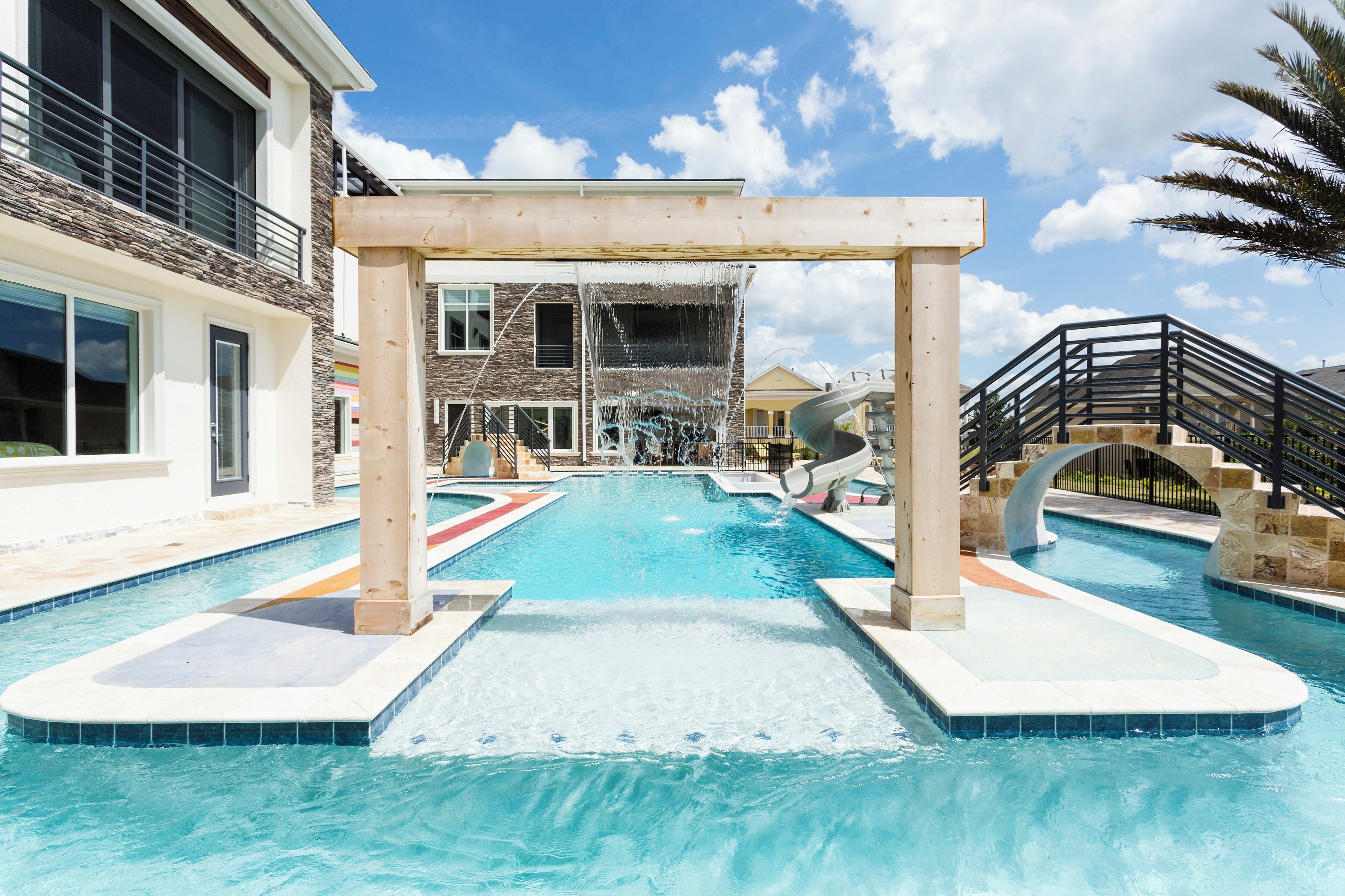 A swimming pool with a water slide, a covered area, and a multi-story building in the background.