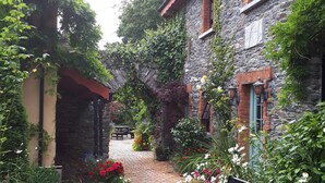 A brick-paved courtyard with a bench, surrounded by stone buildings and lush greenery.