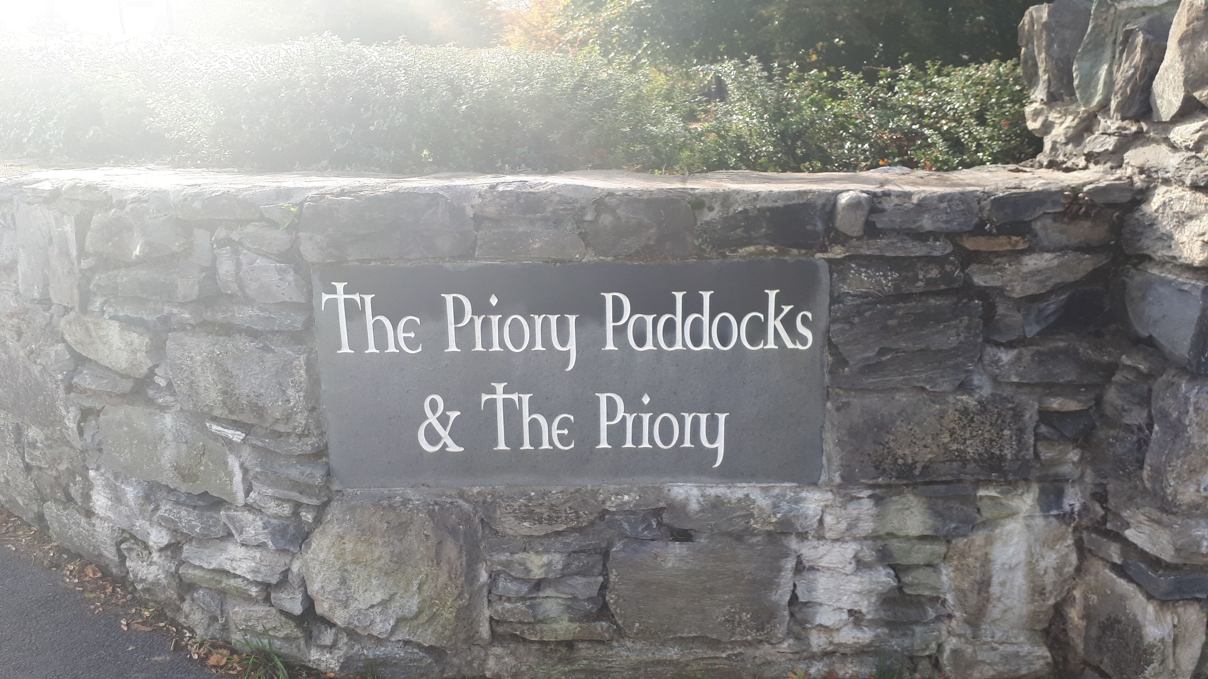 A stone wall with a sign that reads "The Priory Paddocks & The Priory."