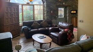 A cozy living room with a stone wall, a large arched window, a leather sofa, a wooden coffee table, and a globe.