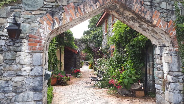 A stone archway leading to a cobblestone pathway lined with potted plants and flowers.