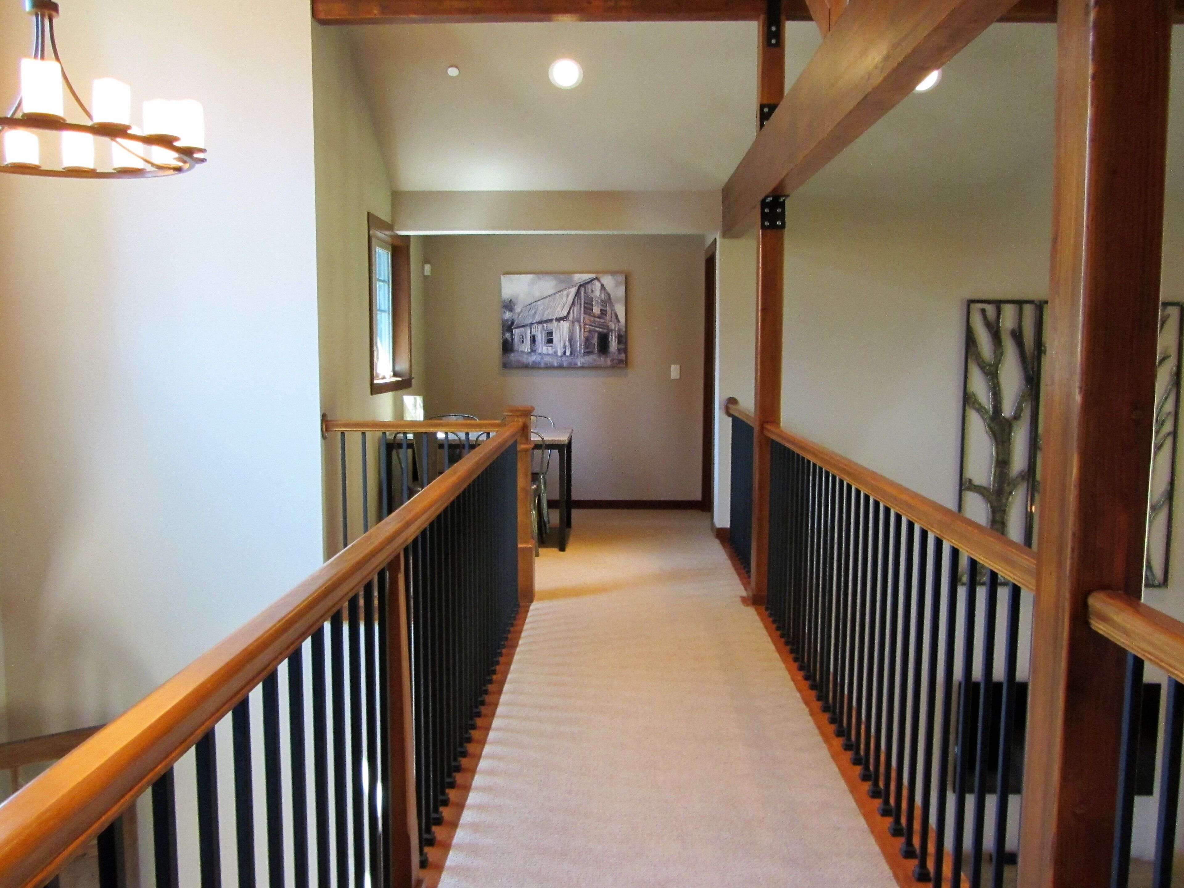 A hallway with a wooden railing, a carpeted floor, and a painting on the wall.