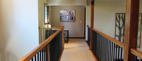 A hallway with a wooden railing, a carpeted floor, and a painting on the wall.