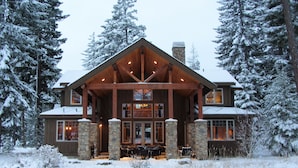 A large, two-story lodge with a stone facade and wooden beams, surrounded by snow-covered trees.