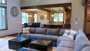 A spacious living room with a sectional sofa, black ottomans, and a large wall clock.
