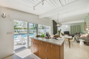 Une cuisine moderne dotée d’un grand îlot central, d’un coin repas avec télévision et d’une vue sur une piscine.