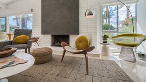 Ein modernes Wohnzimmer mit Kamin, einem runden Couchtisch und zwei Sesseln mit Kissen.