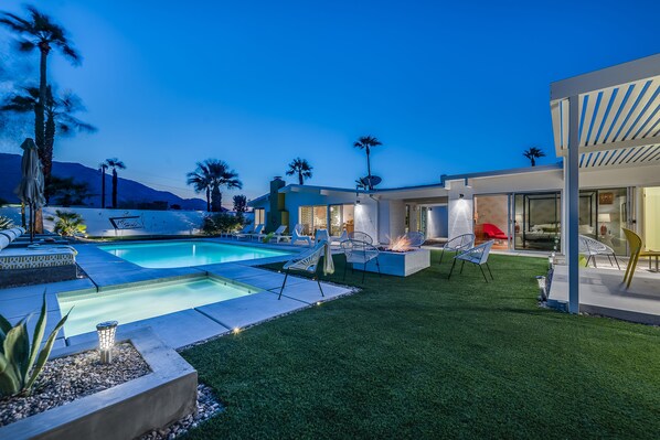 Un espace piscine extérieur moderne, doté d’une pelouse bien entretenue, de chaises longues et d’un foyer.