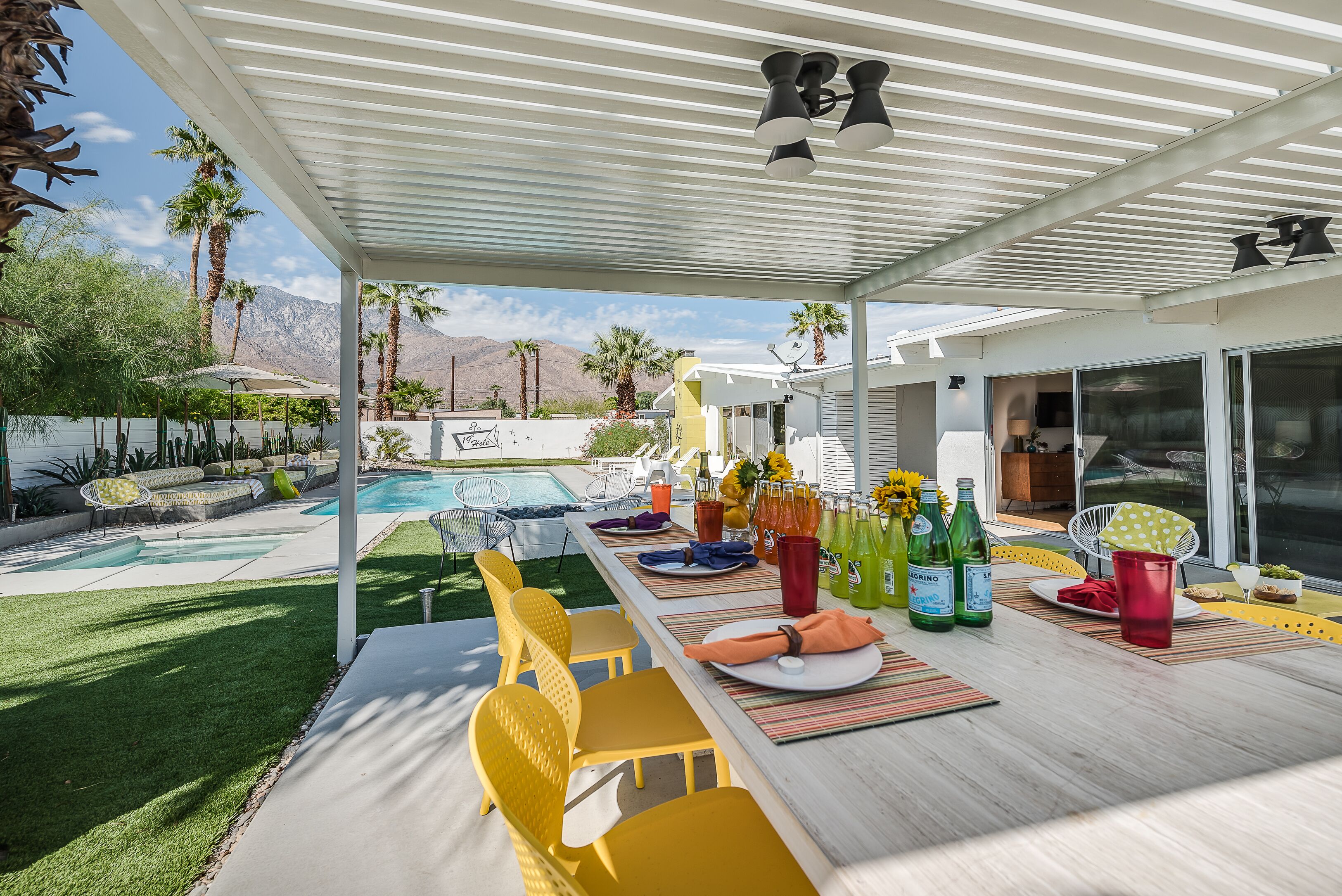 An outdoor patio with a pool, yellow chairs, and a dining table set for a meal.