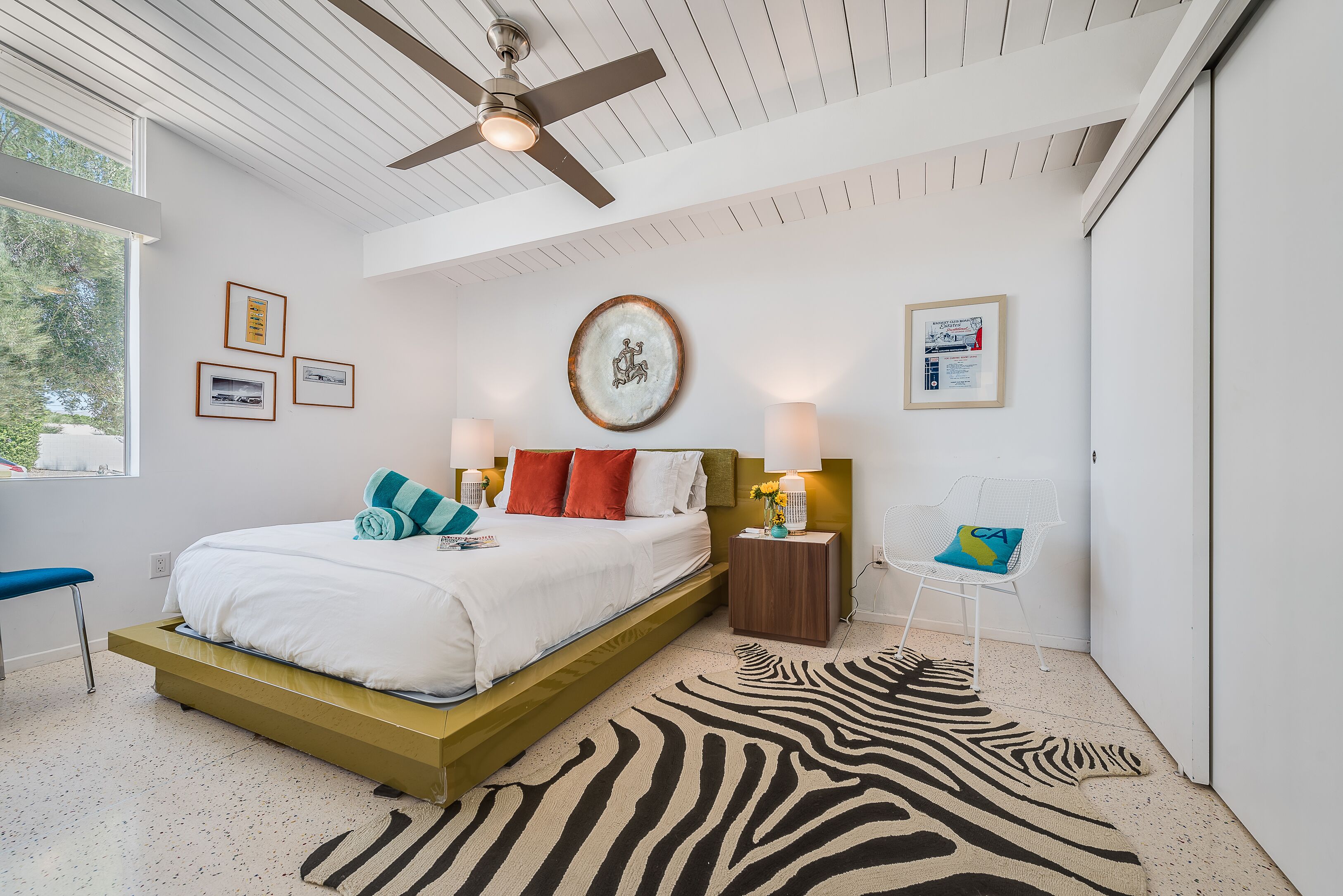 Un dormitorio moderno con cama, lámparas de noche, un felpudo con estampado de cebra y cuadros en la pared.
