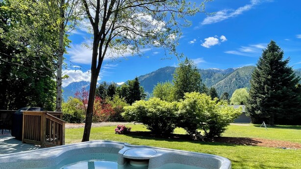 Un jacuzzi en un jardín con montañas al fondo.