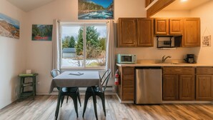 Cocina con armarios de madera, microondas y lavavajillas. Se ve una ventana con vistas a árboles y un río.