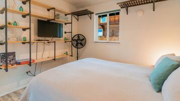 A bedroom with a bed, a TV mounted on a shelf, a window, and a fan.