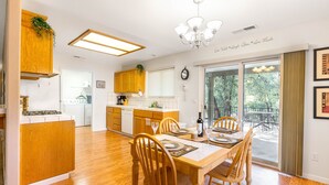 A modern kitchen with wooden cabinets, a dining area with a wooden table and chairs, and a view of the outdoors through large windows. - Riverside Manna, "Gateway to Beautiful Yosemite Valley" Modern 3bd/2 ba cottage (Mariposa)