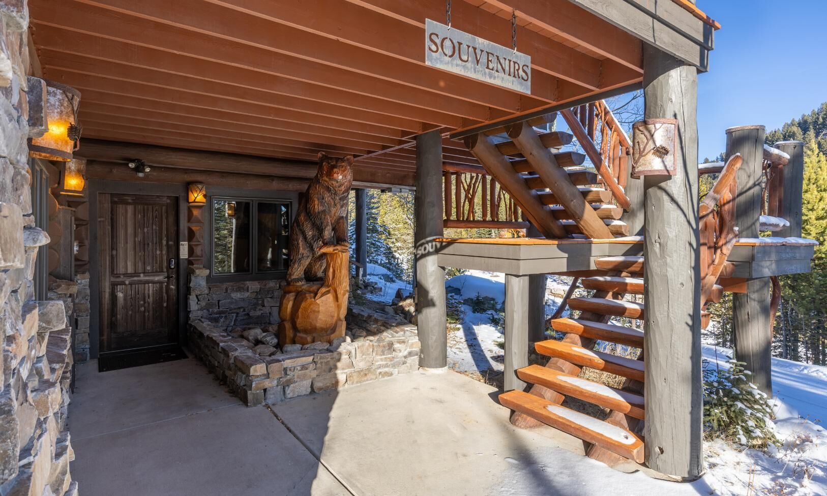 A wooden staircase leading to a covered entrance with a bear sculpture and a sign reading "SOUVENIRS".
