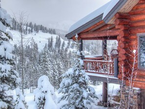 Eine Blockhütte mit einer Holzterrasse und Blick auf schneebedeckte Bäume und Berge.