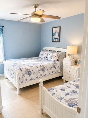 A bedroom with a bed, a nightstand, a lamp, a ceiling fan, and a framed picture on the wall.