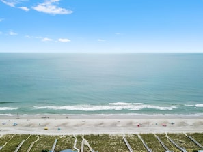 A beach with a clear sky, calm sea, and a sandy shore with people and umbrellas.