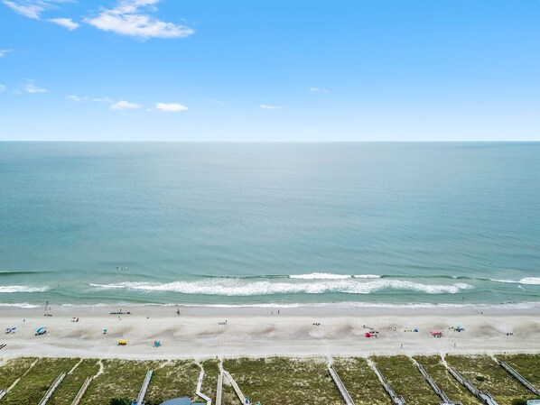 Ein Strand mit blauem Himmel, ruhiger See und Sandstrand, an dem sich Menschen und Sonnenschirme befinden.