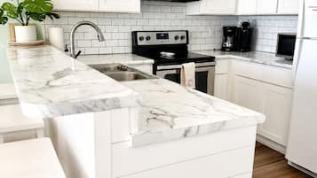 Una cocina con muebles blancos, encimera de mármol, estufa de acero inoxidable y horno empotrado.