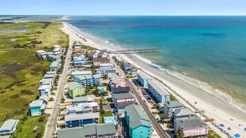 An aerial view of a coastal town with beachfront properties, a pier, and a road leading to the beach.